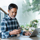 Man looking at phone while working on laptop